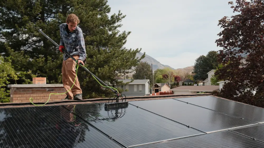 Canyon Clear technician washing a rooftop residential solar panel array with a water-fed soft-bristle brush in Utah County